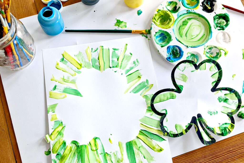 Children painting shamrocks at a library activity table.